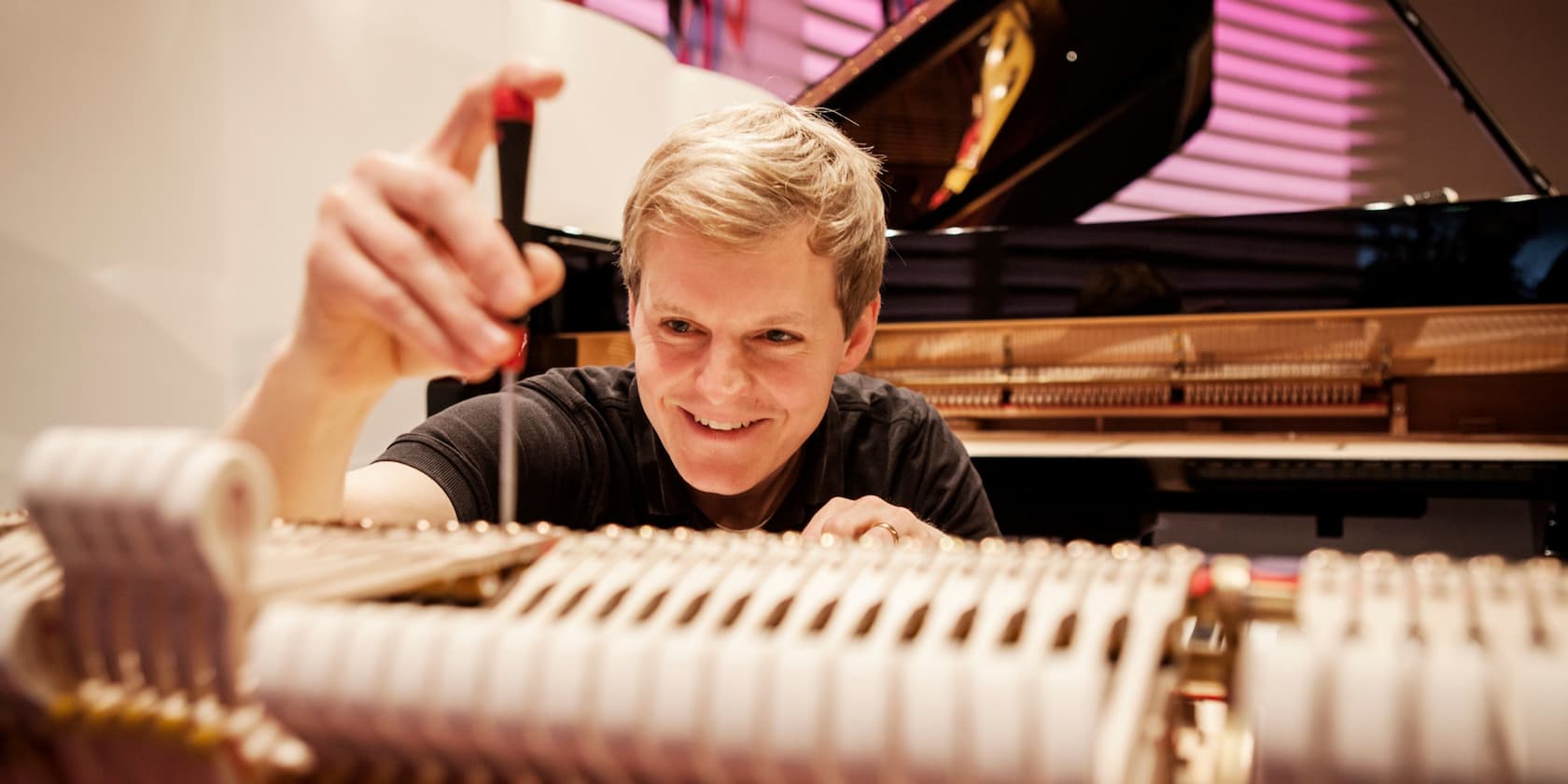 A smiling man is repairing the inside of a piano.