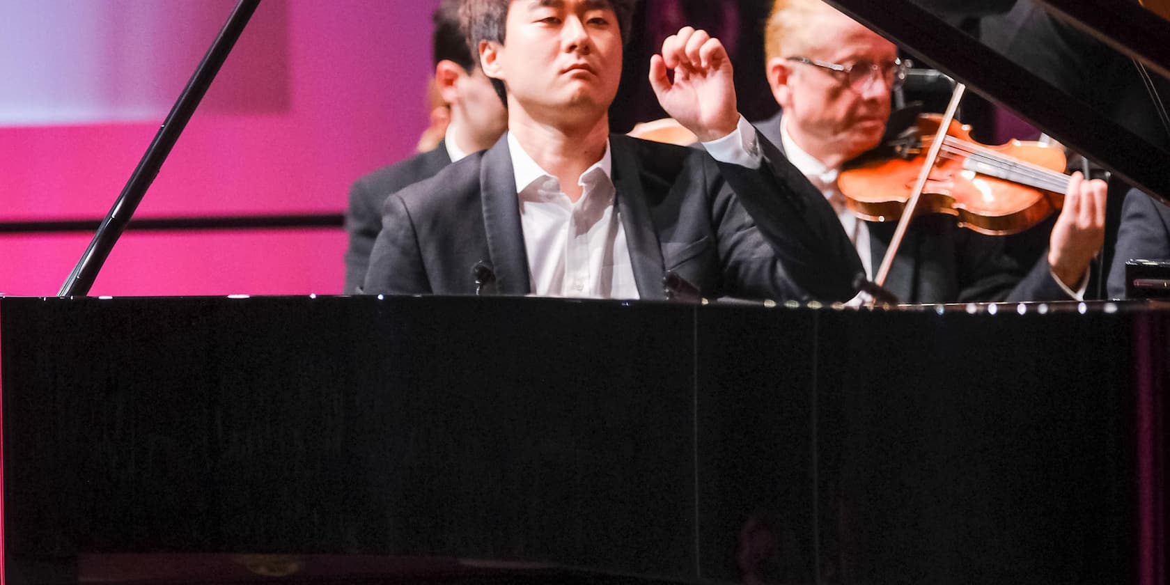 A pianist plays the piano while a violinist plays in the background.