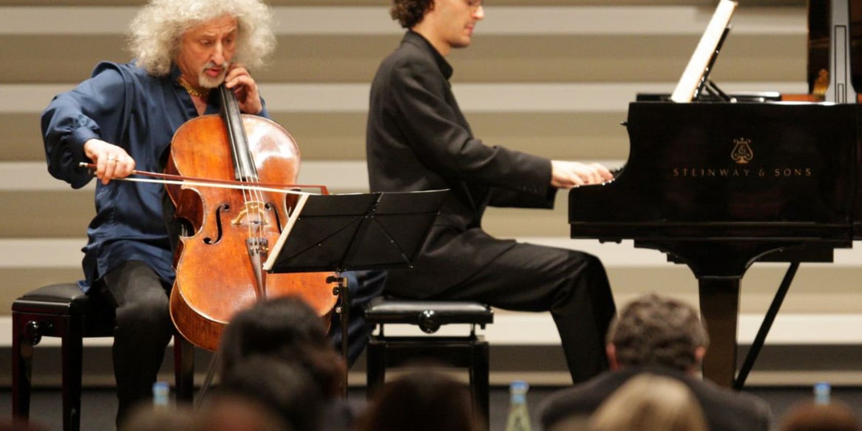 A cellist and a pianist perform on stage in front of an audience.