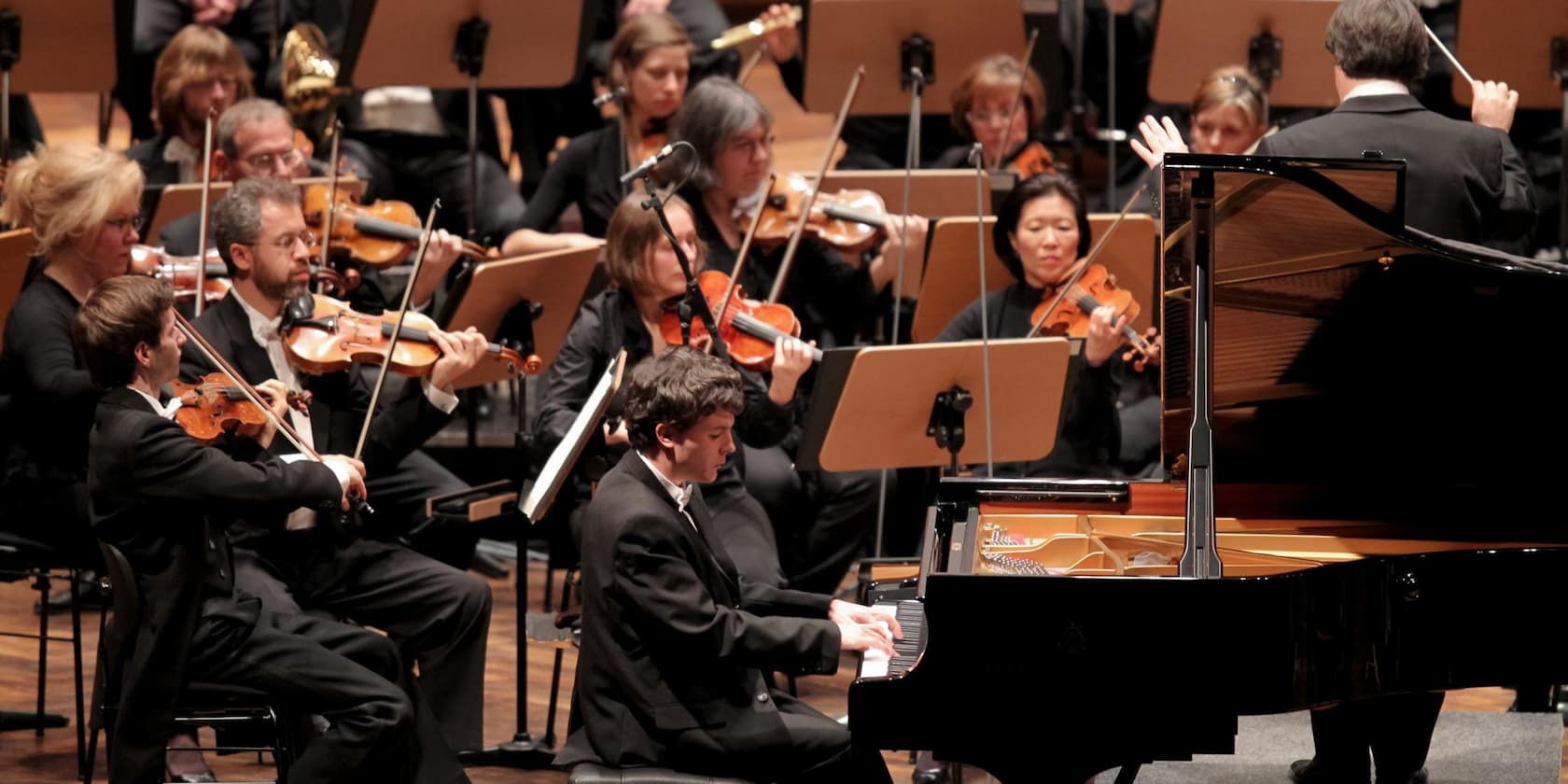 An orchestra playing on stage, with a pianist seated in the center at the piano.