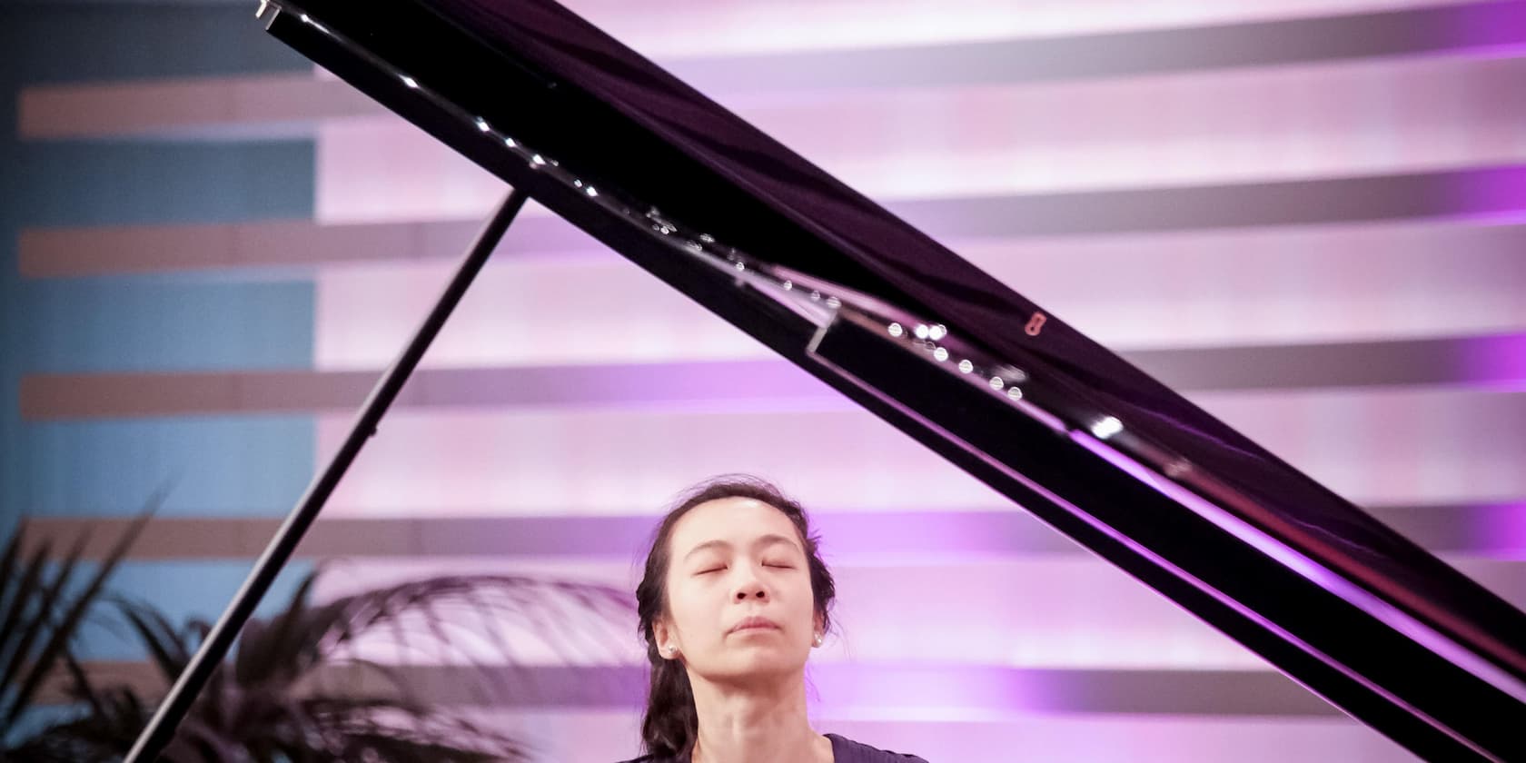 A woman plays the piano with concentration on a stage with purple lighting.