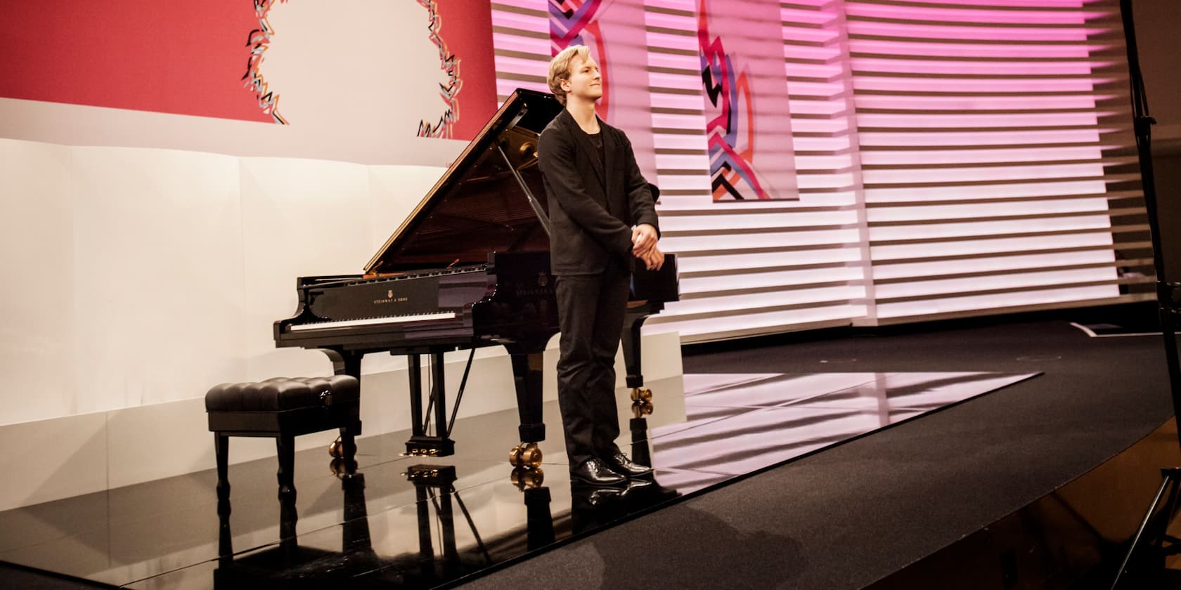 A pianist stands next to a grand piano on a stage.