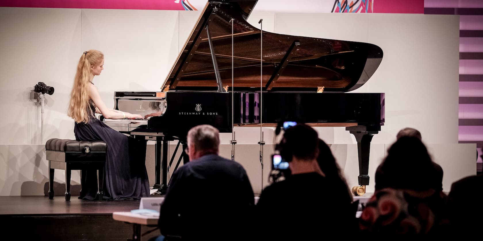 A woman playing piano on a stage in front of an audience.