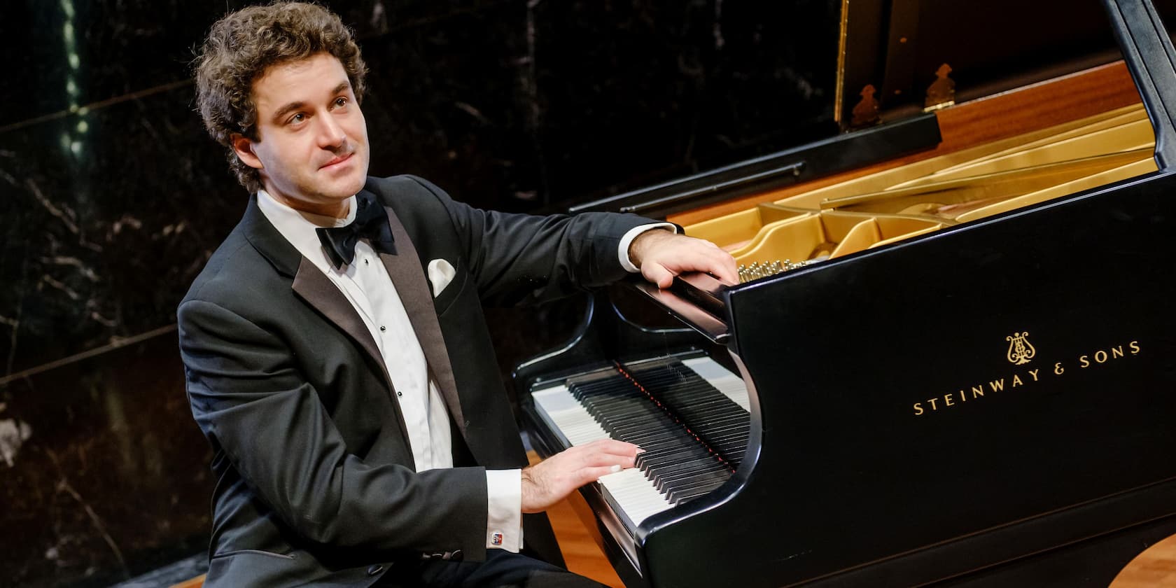 A man in a tuxedo playing a Steinway & Sons grand piano.