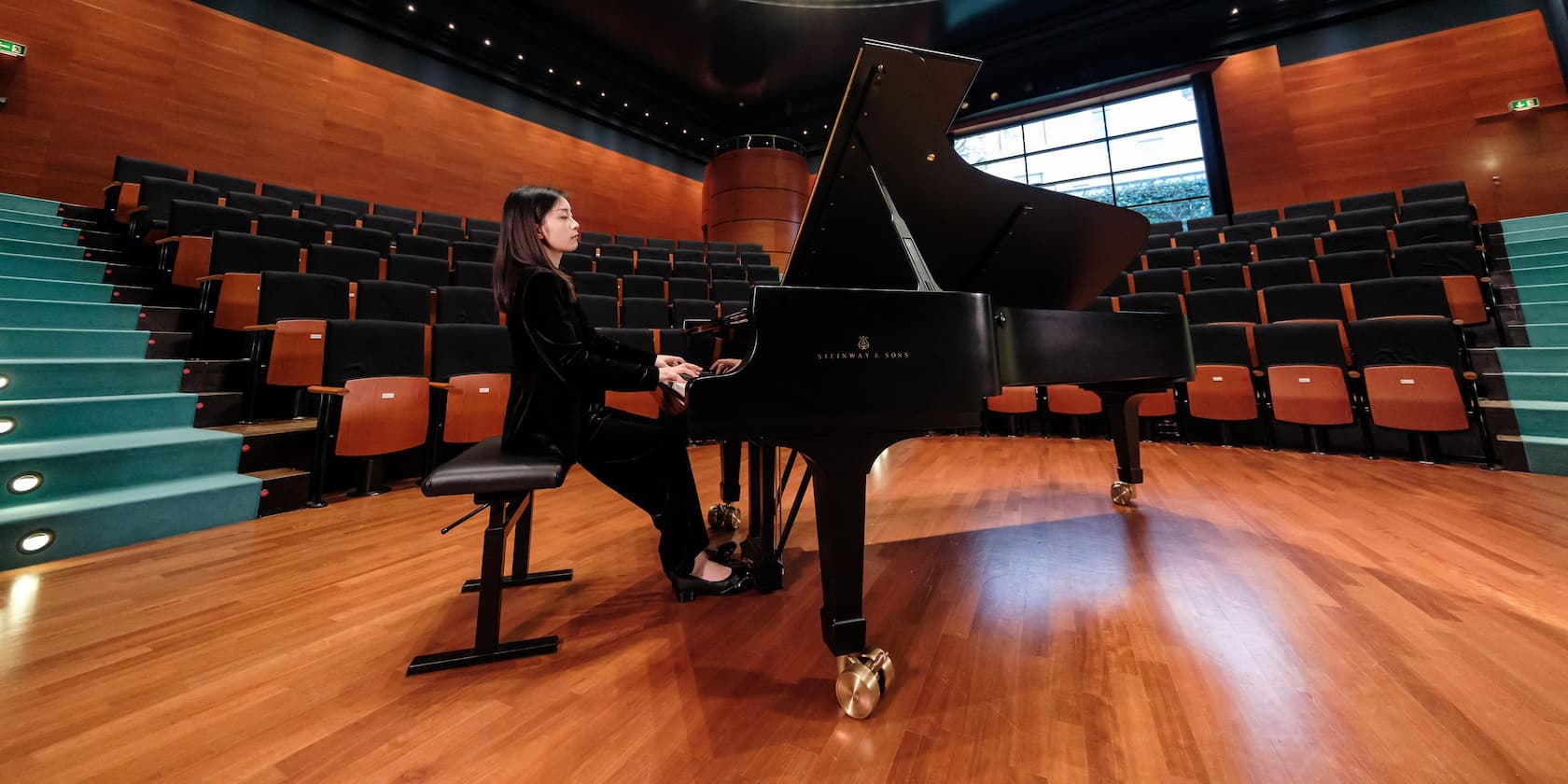 A woman playing piano on a stage in an empty concert hall.