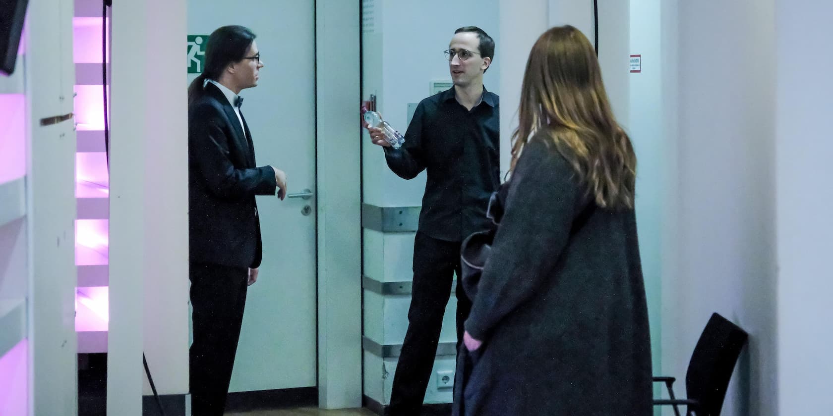 Three people conversing in a hallway, one person holding a water bottle.