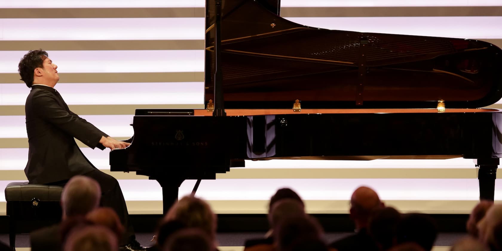 A pianist playing on a grand piano in front of an audience.