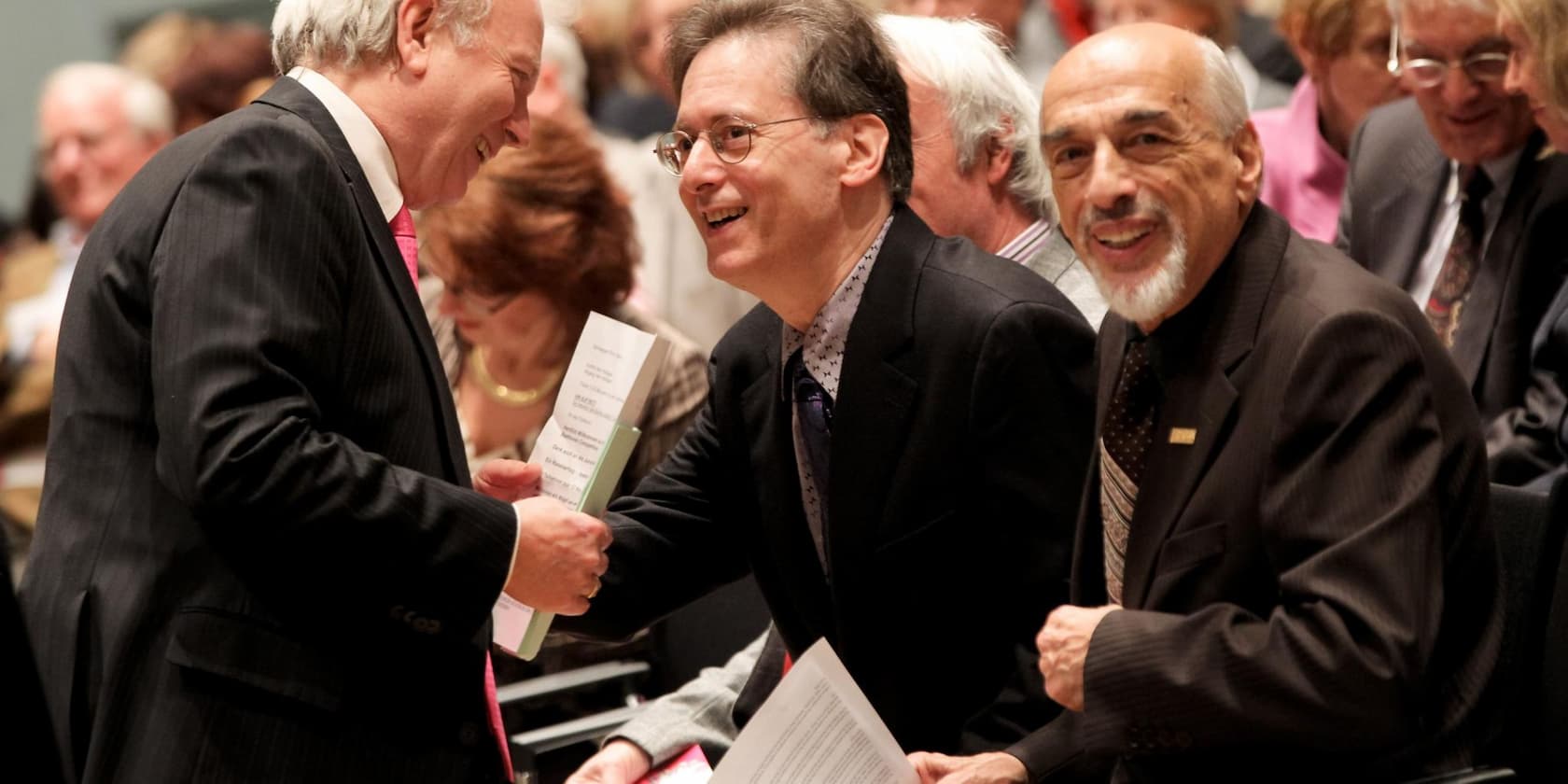 Three men in suits conversing and smiling at an event.