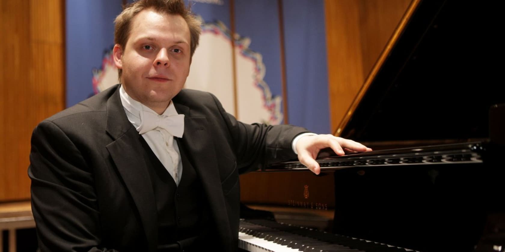 A man in a tuxedo sitting by a grand piano.