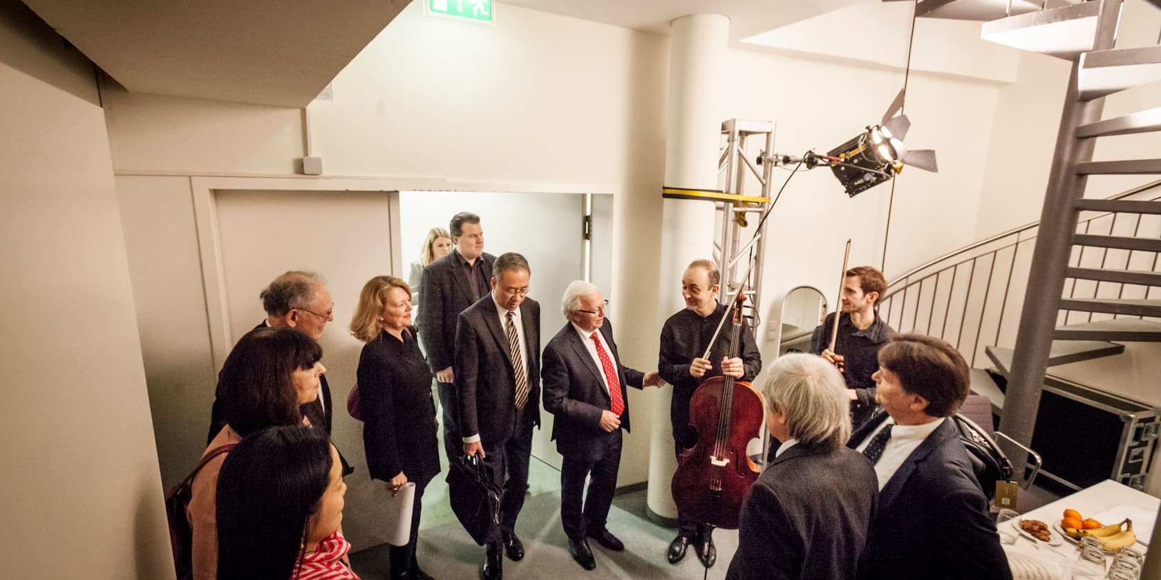 A group of people, including a man with a cello, stand in a modern room.