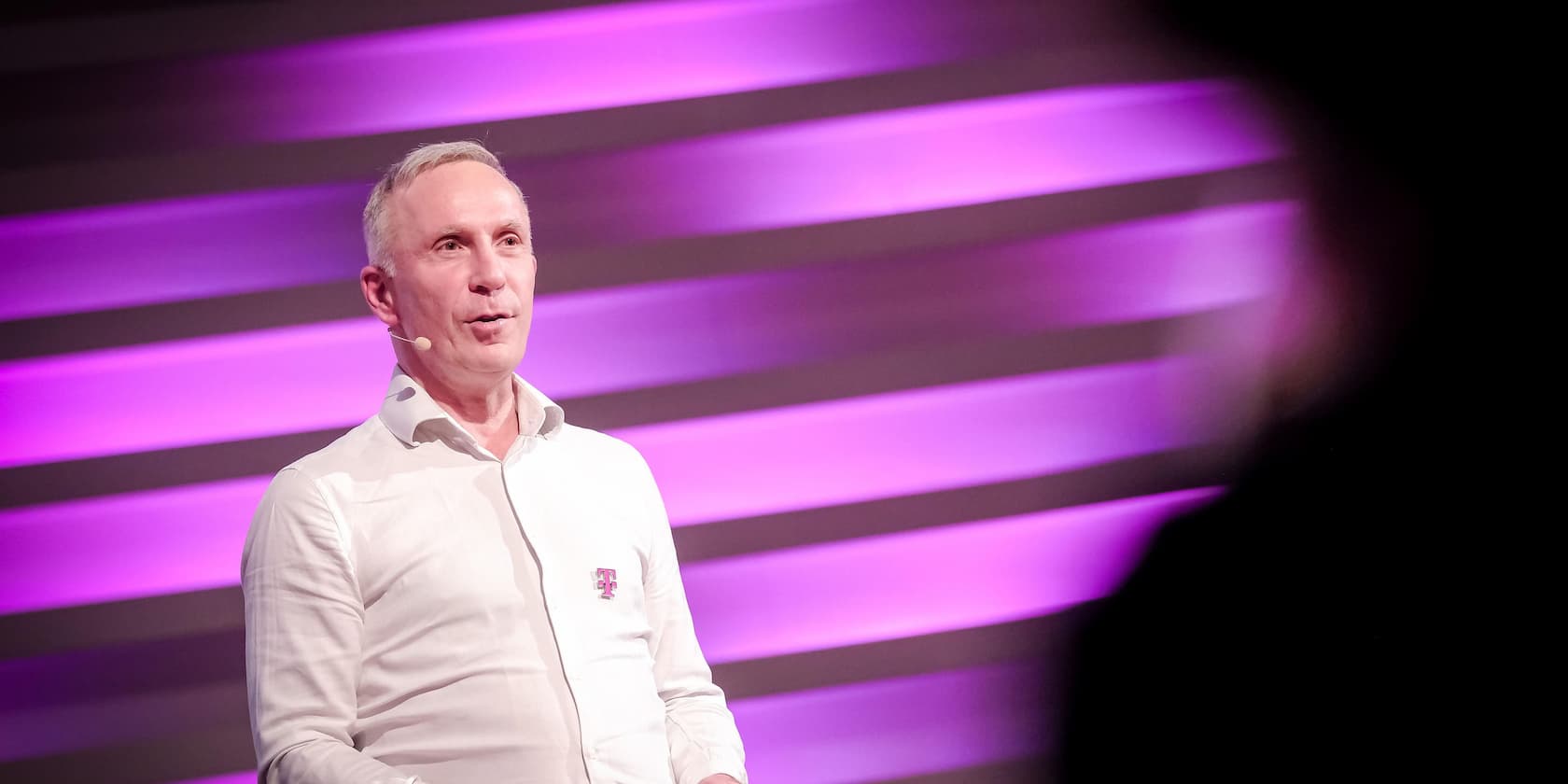 A man speaks on a stage in front of a purple-lit background.