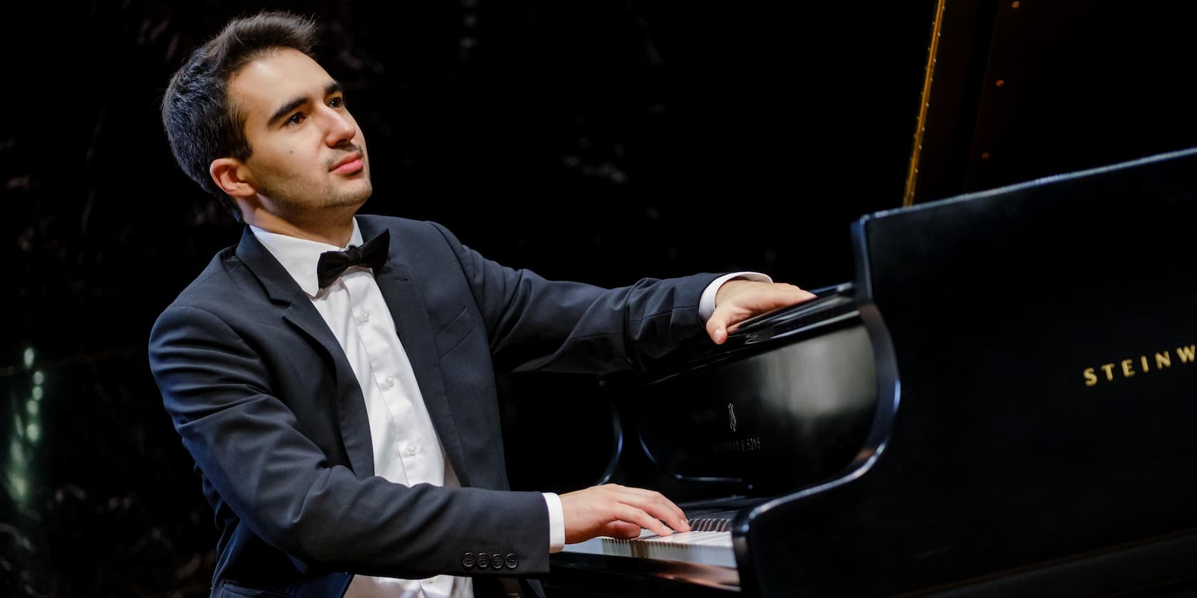 A man in a suit playing the piano on stage.