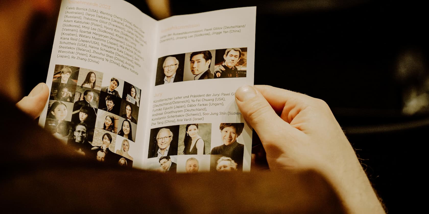 A person holds a program booklet with photos and names of participants and jury members of a competition.