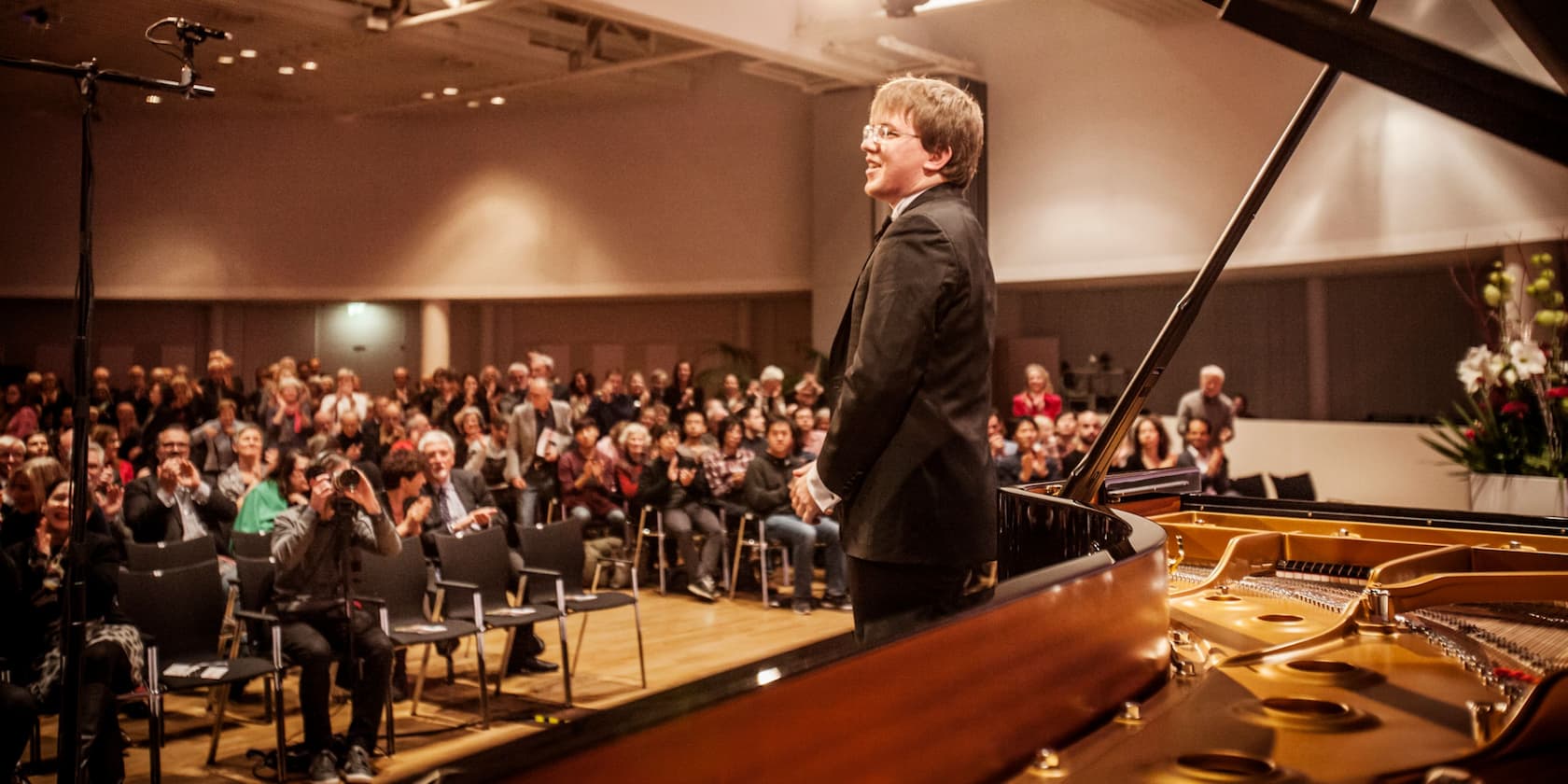 A pianist bows to a standing audience in a concert hall.