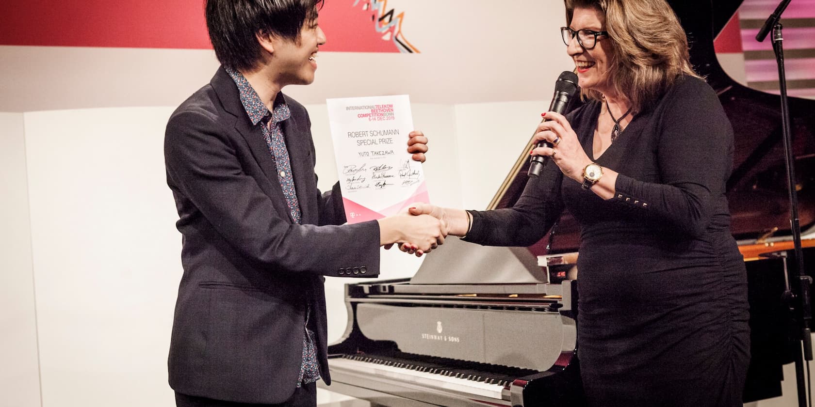 A man receives a certificate for the Robert Schumann Special Prize while shaking hands with a woman.