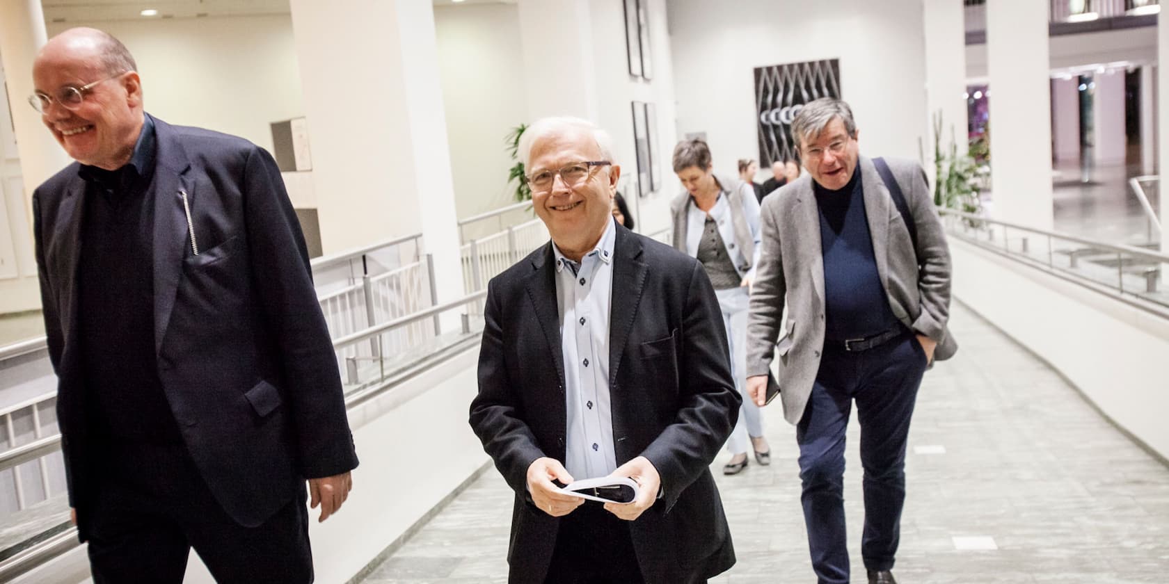 Three men and one woman walking through a bright office corridor.