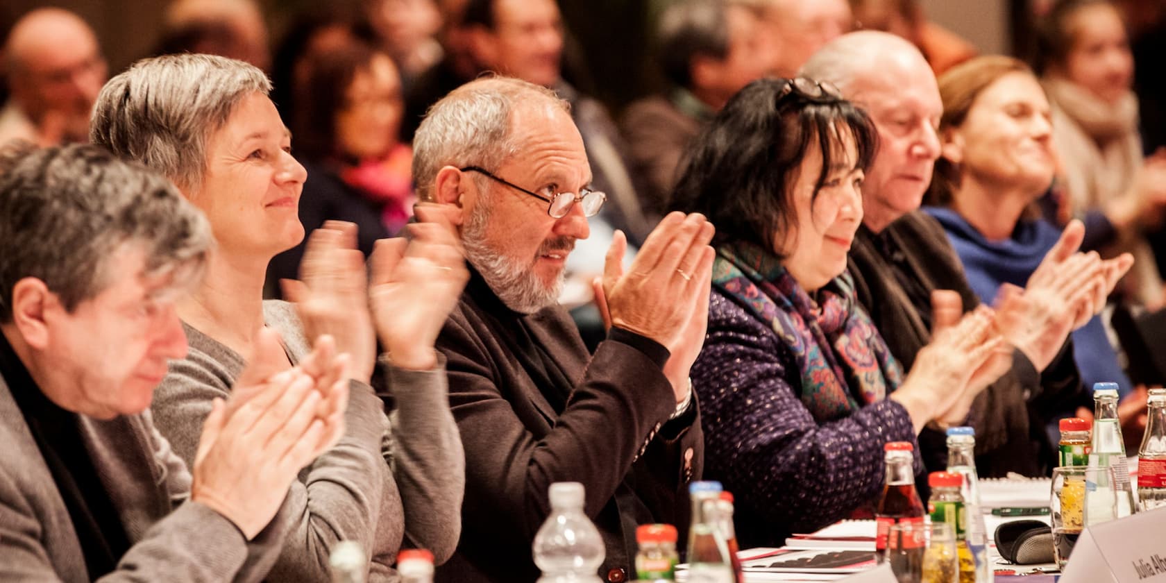 Menschen applaudieren an einem Konferenztisch.