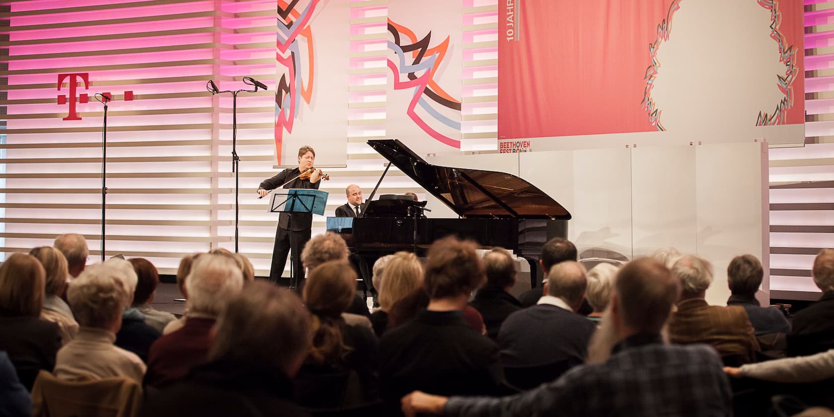 A violinist and a pianist perform at a Beethovenfest event in front of an audience.