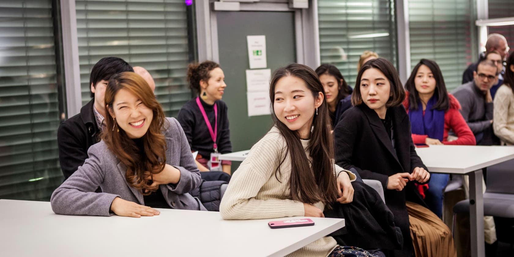 A group of people smiling and conversing while sitting at a table in a modern room.