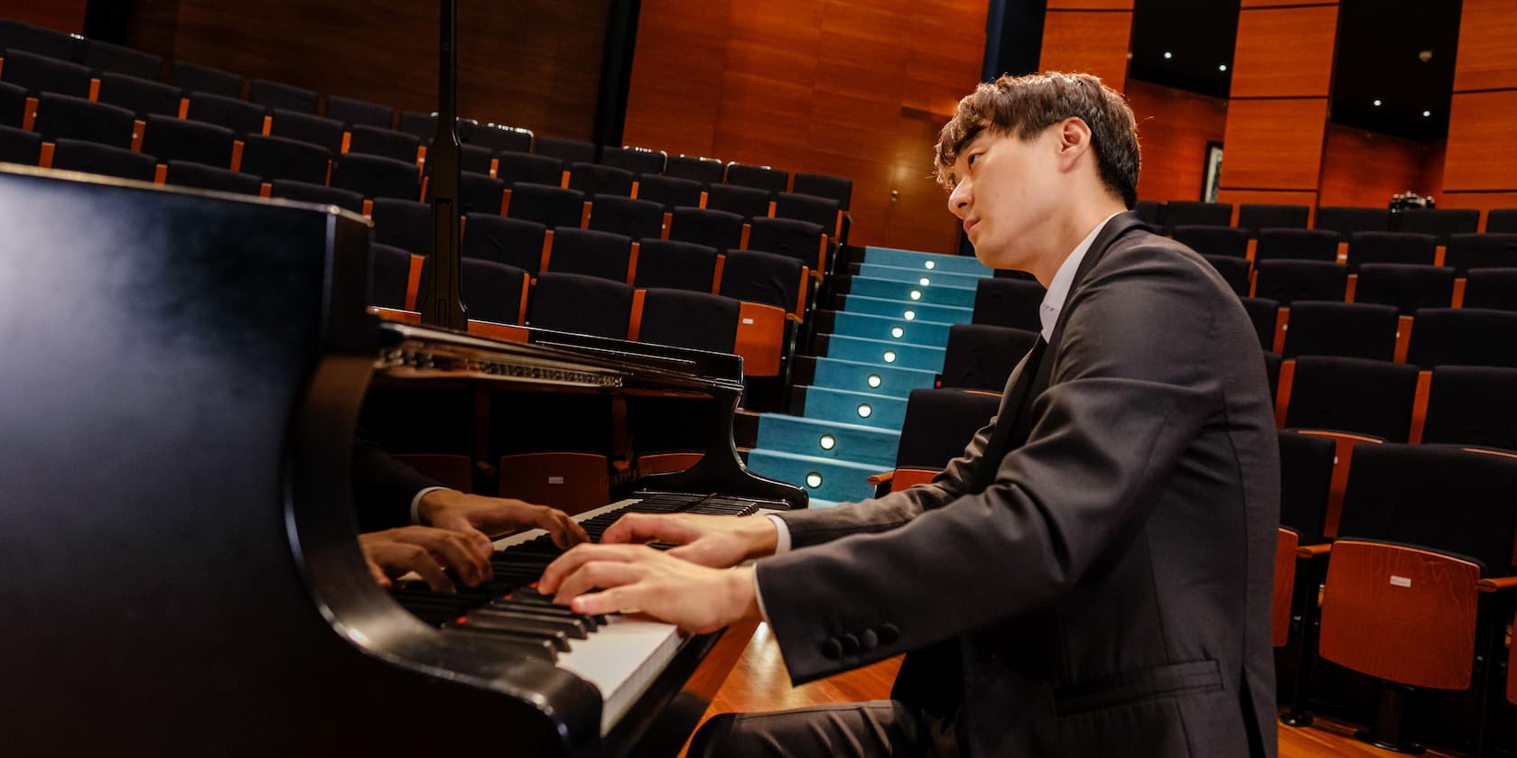 Man in a suit playing piano in an empty concert hall.