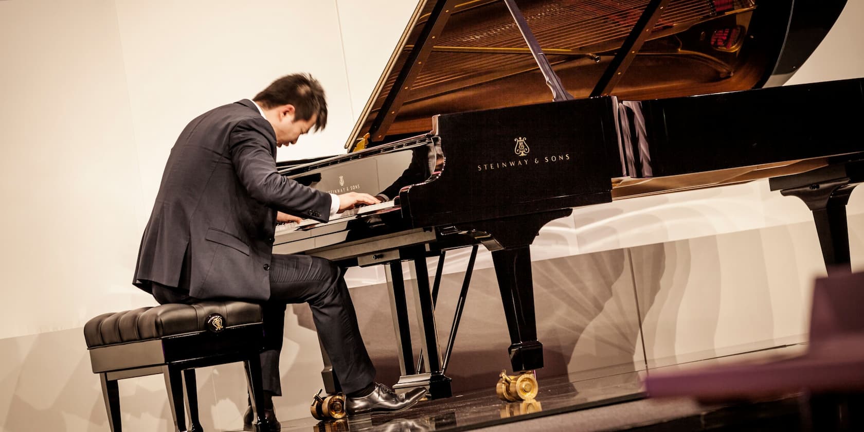 A man in a suit playing a Steinway & Sons piano.