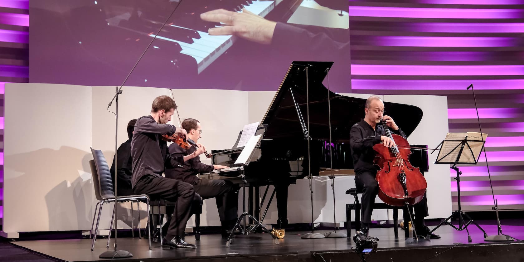 Three musicians play cello, piano, and violin during a performance.