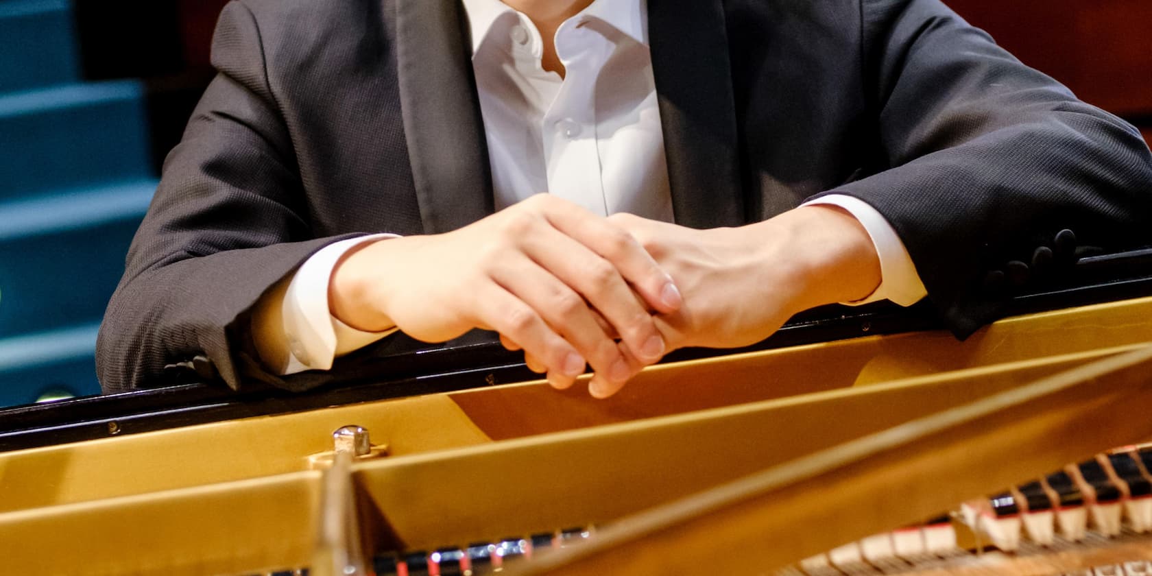 Hands of a person in a suit, folded over a piano lid.