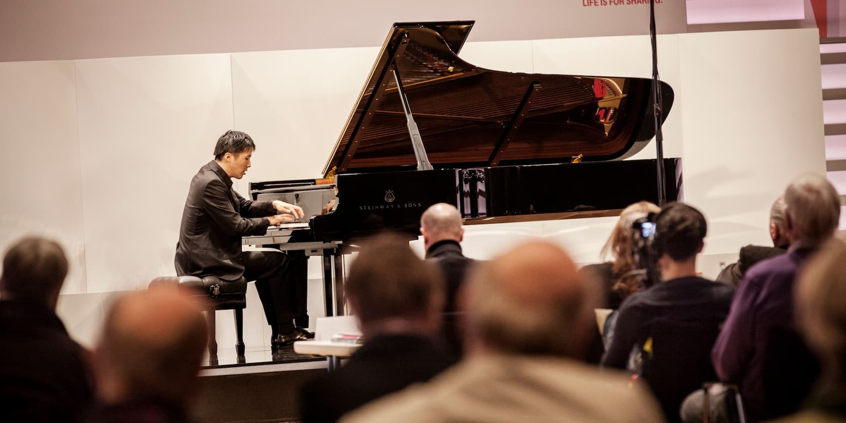 A pianist plays on a grand piano in front of an audience.