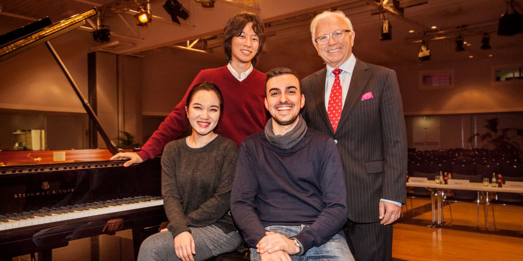 Vier Personen posieren lächelnd neben einem Steinway & Sons Flügel.