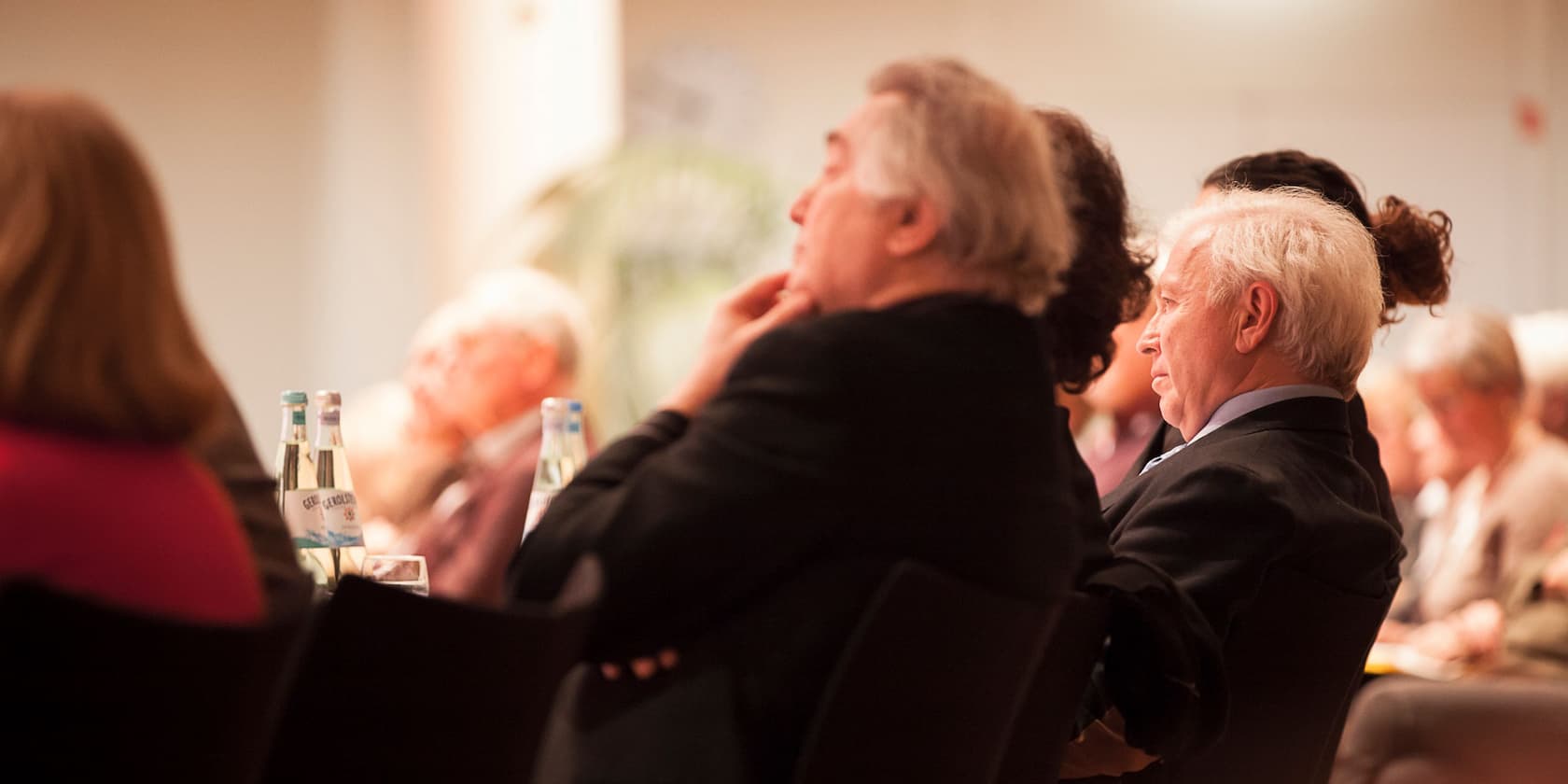 People sitting and listening, some with water bottles on the table.