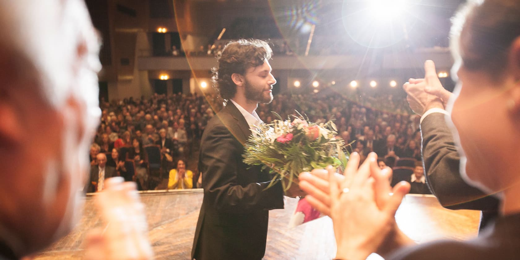 A man with a bouquet of flowers on a stage being applauded by an audience.