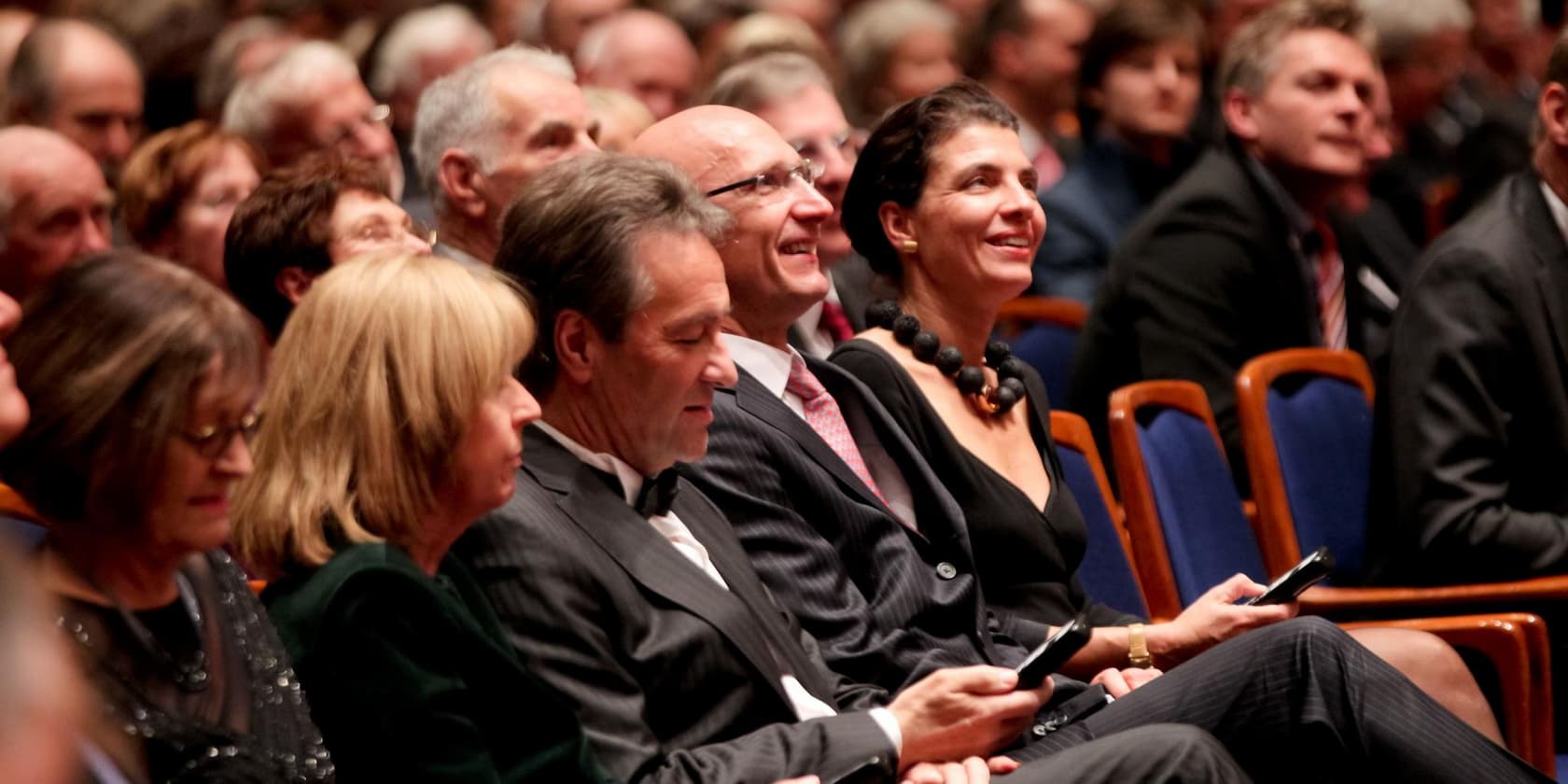 Group of people seated in an auditorium, some smiling and looking forward.