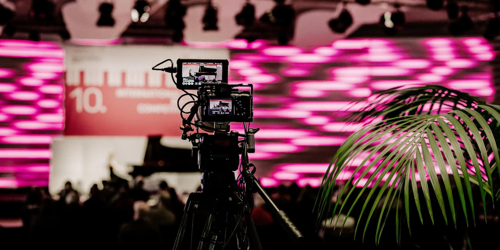 Camera filming an event with a lit stage background in pink.