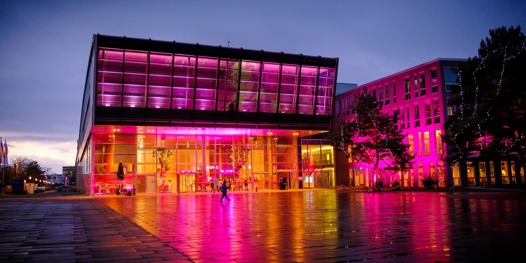 A modern building illuminated with magenta lighting at dusk.