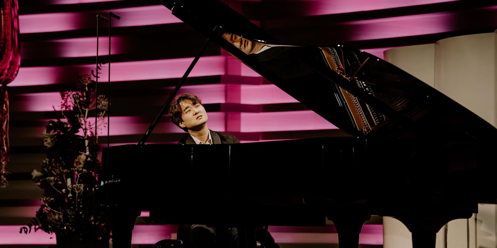 A man playing piano in front of a backdrop with pink lighting.