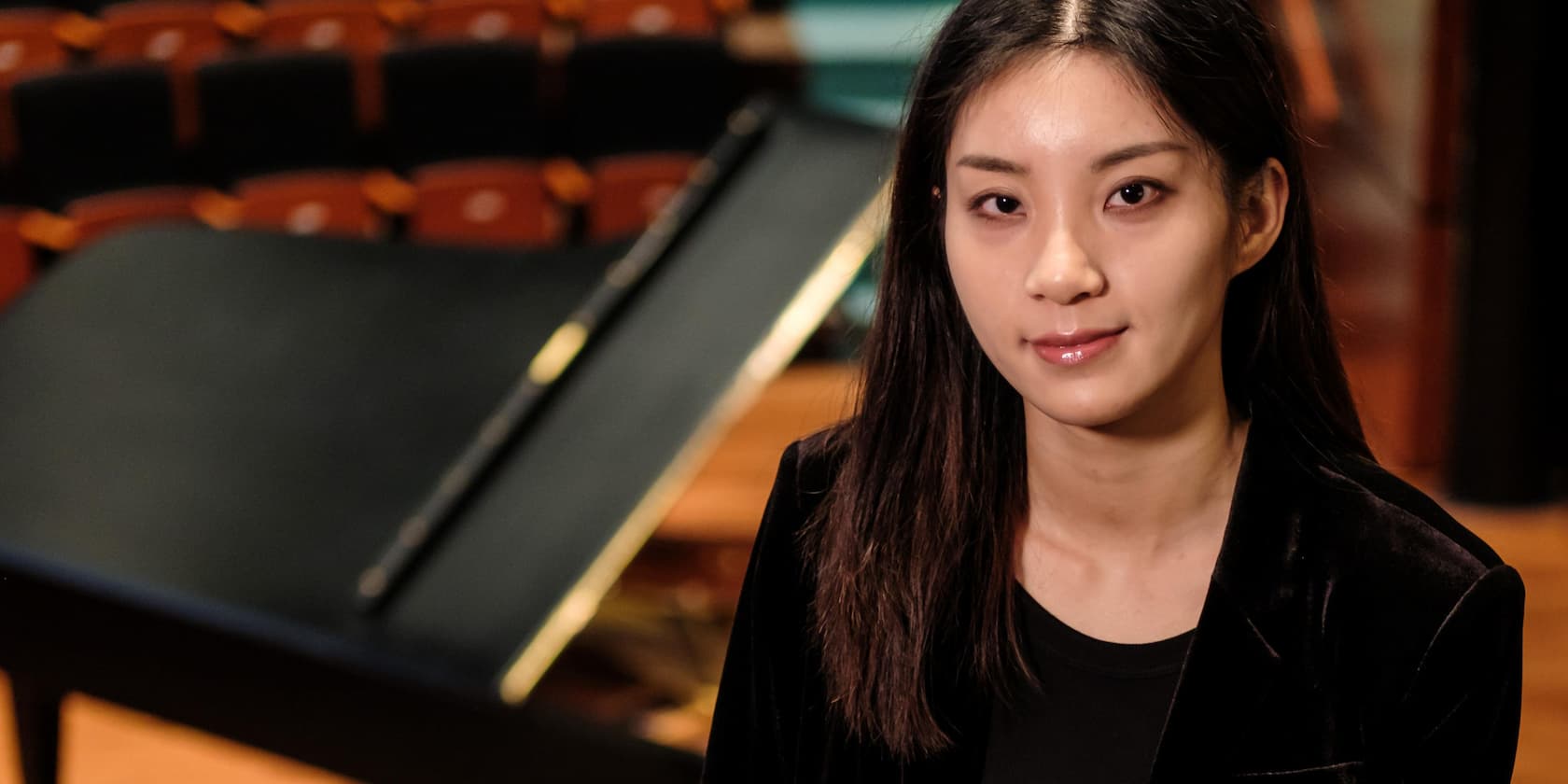 A woman sits in a concert hall, with a piano in the background.