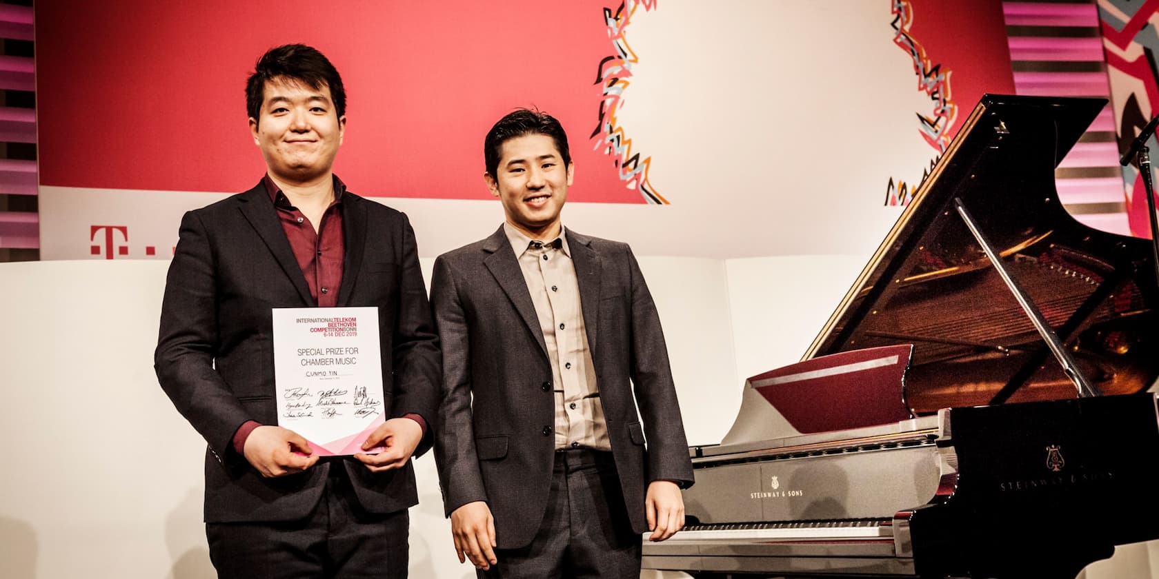 Two men standing next to a piano. One is holding a certificate for the Special Prize for Chamber Music.