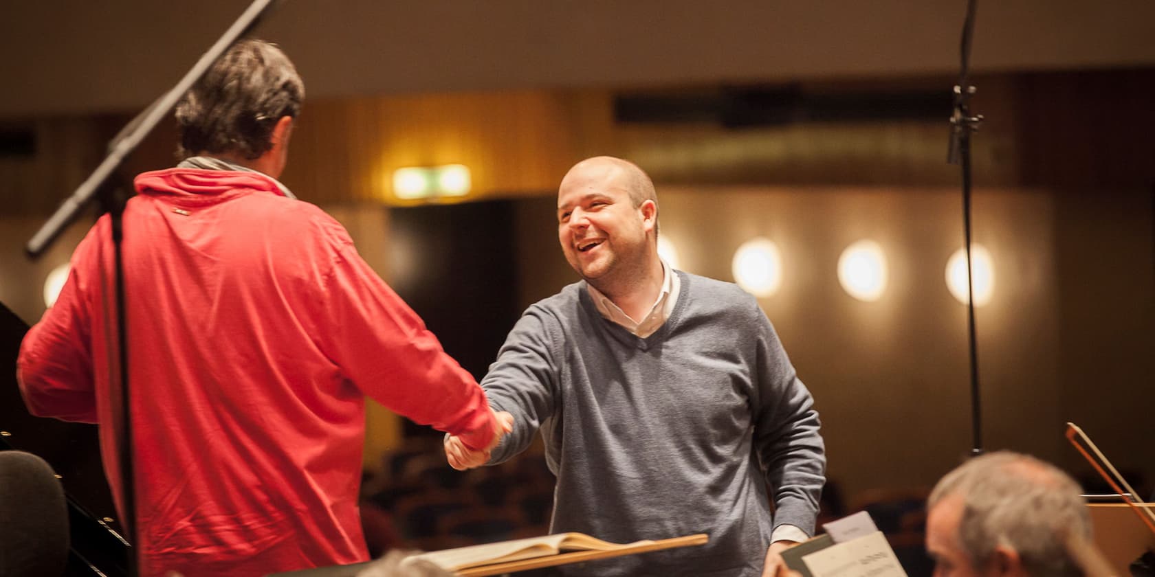 Two men shaking hands and laughing in a concert hall.