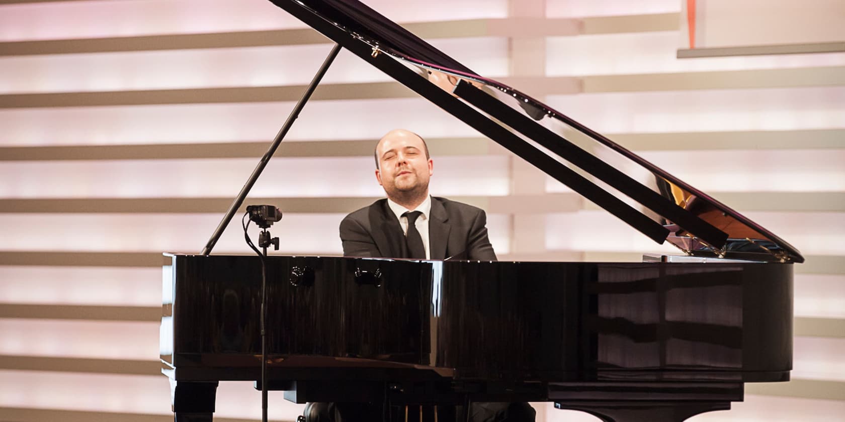 A man in a suit playing the piano on a stage.