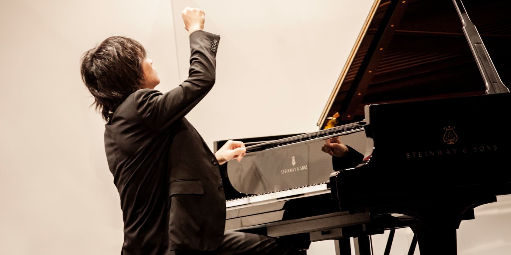 A pianist is playing on a Steinway & Sons grand piano and raising his hand.