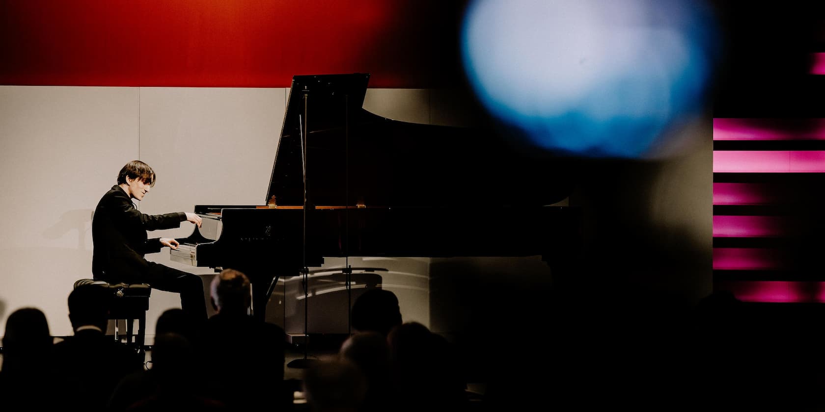 Man playing piano on a stage with a red and white background.