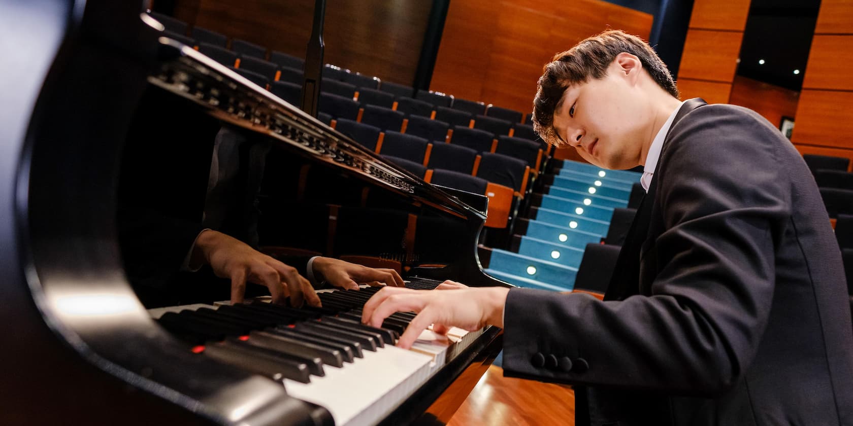 A man in a suit playing the piano in an empty concert hall.