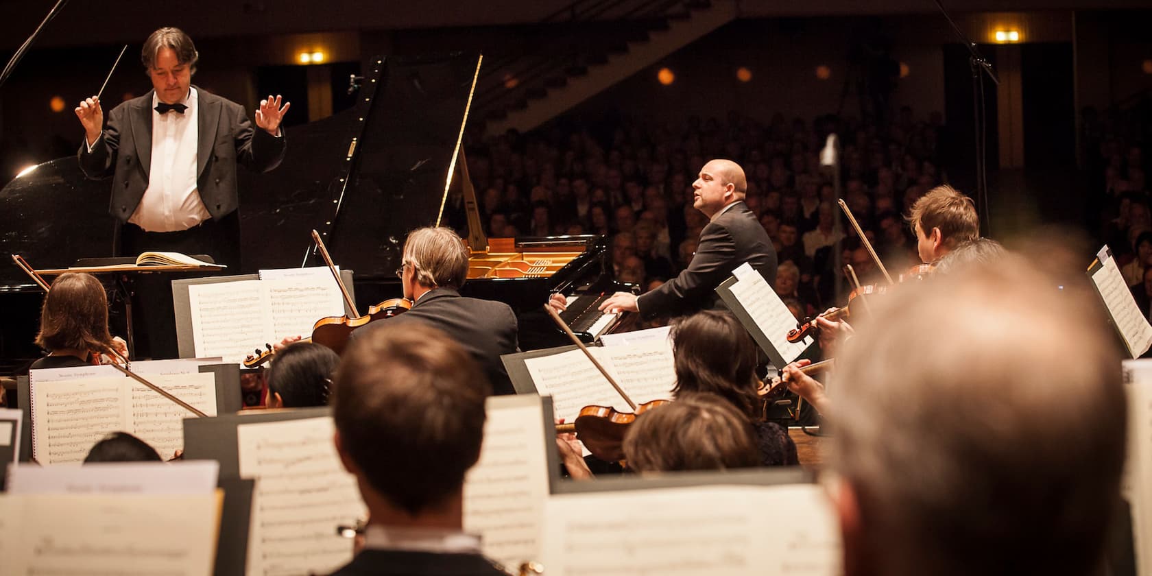 Conductor and pianist leading an orchestra in a concert hall.