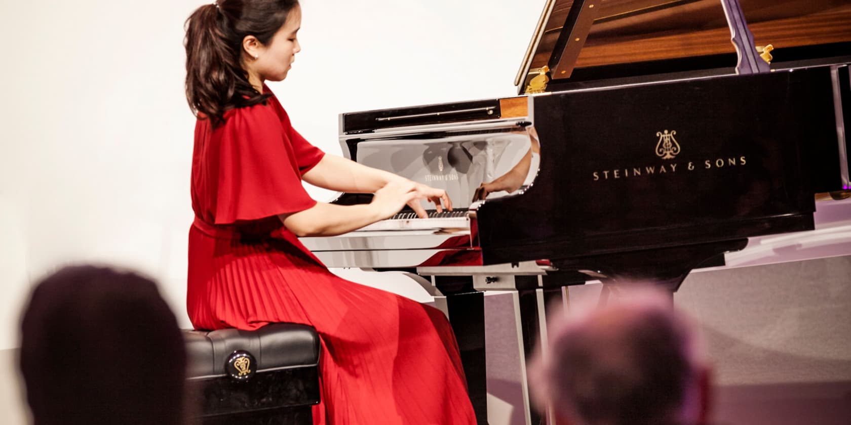 Frau in einem roten Kleid spielt Klavier auf einer Bühne