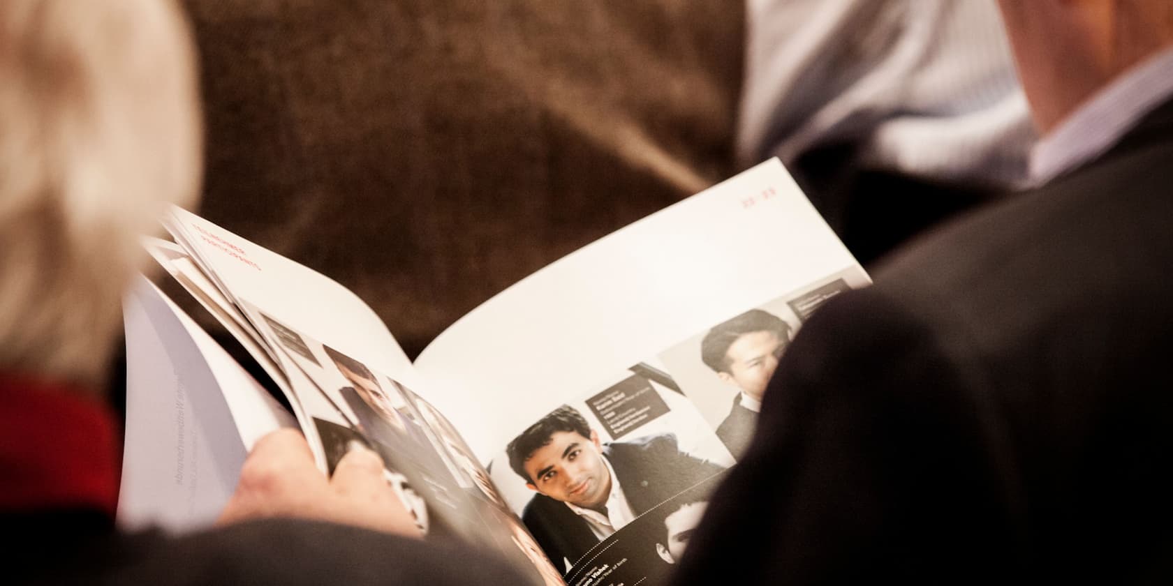 Person reading a brochure with photos of different people.