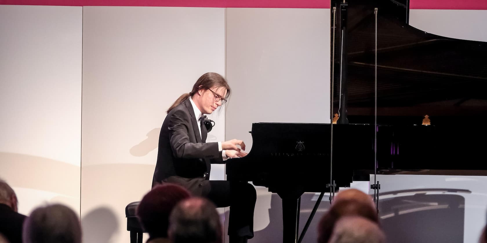 A musician in a suit playing the piano at an event in front of an audience.