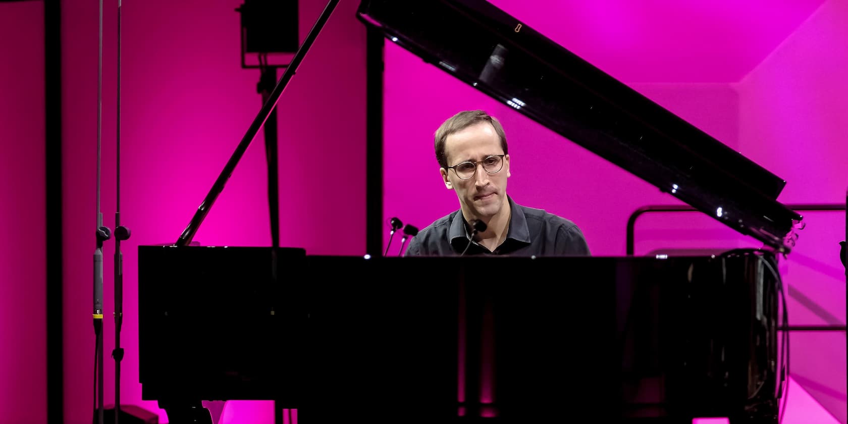 A man playing piano in front of a pink-lit background.