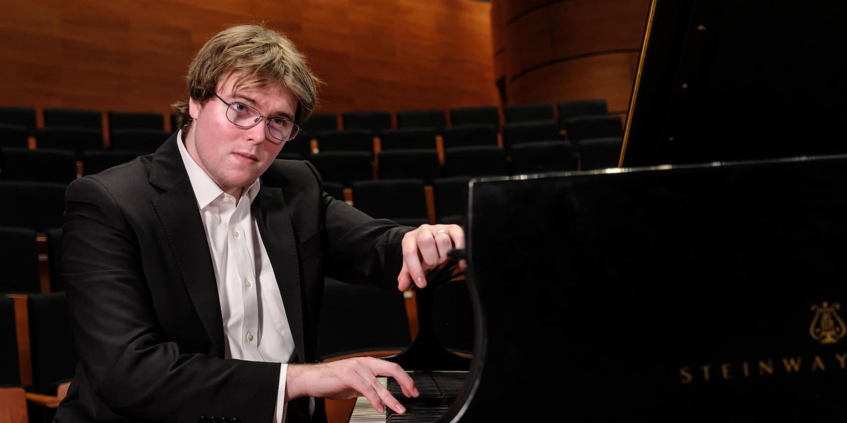 A man in a suit playing the piano in a concert hall.