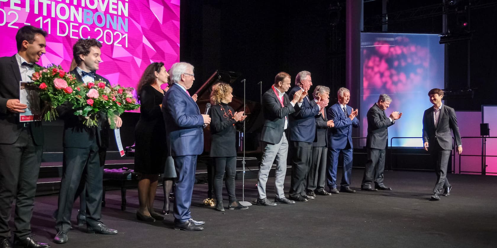 Teilnehmer und Juroren des Beethoven-Wettbewerbs Bonn 2021 stehen auf der Bühne. Zwei Teilnehmer halten Blumensträuße.