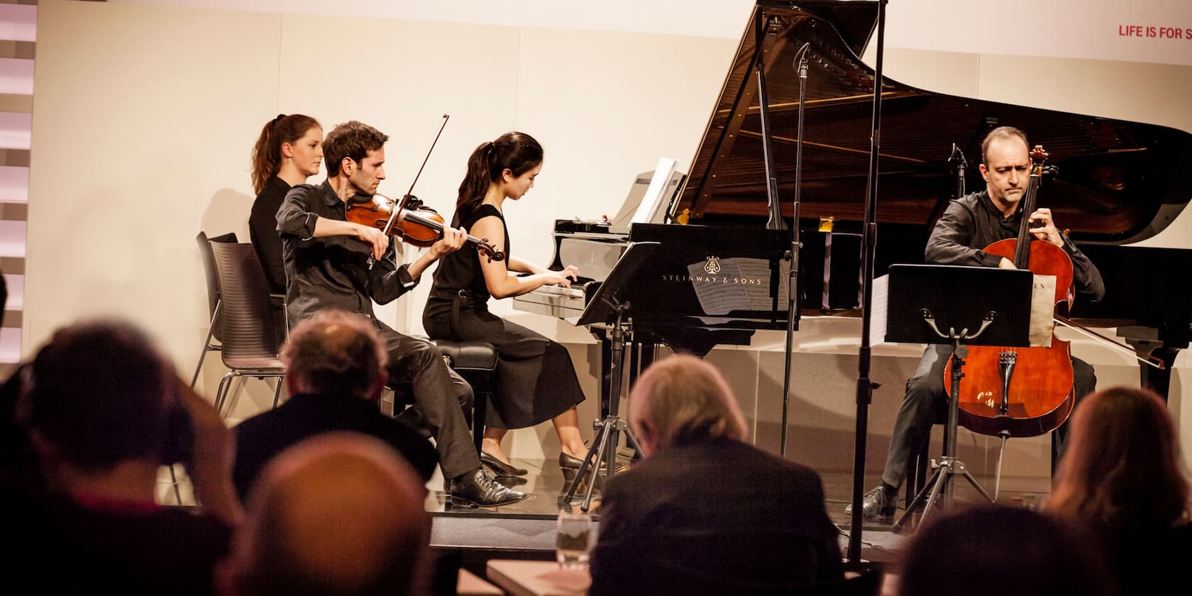 A piano quartet performs in front of an audience.